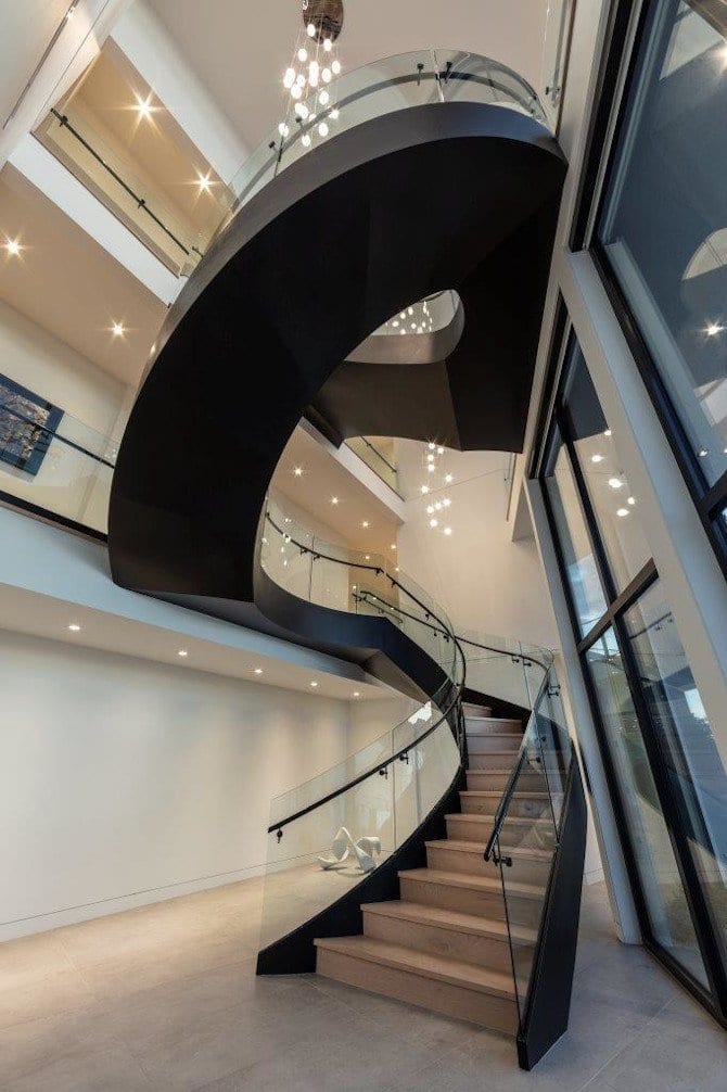 Contemporary spiral staircase with glass railing in a modern building.